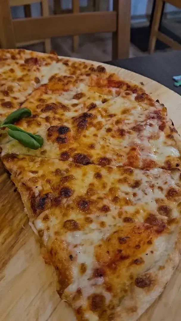 Serowa pizza z przypieczoną skórką i bazylią na drewnianej desce